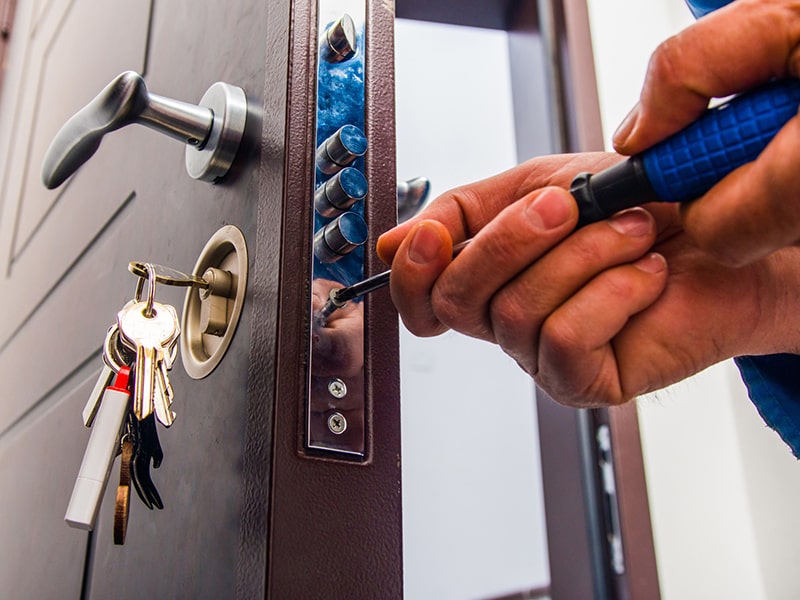 Fotografía de una puerta con llaves introducidas y las manos de un cerrajero desatornillando un pomo.