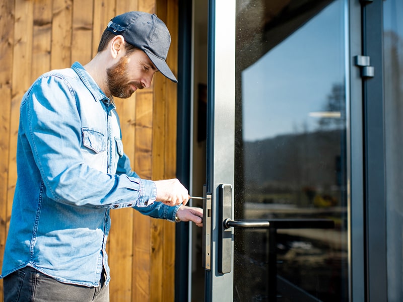 Fotografía de un cerrajero utilizando un destornillador en el cerrojo de una puerta con cristalera.